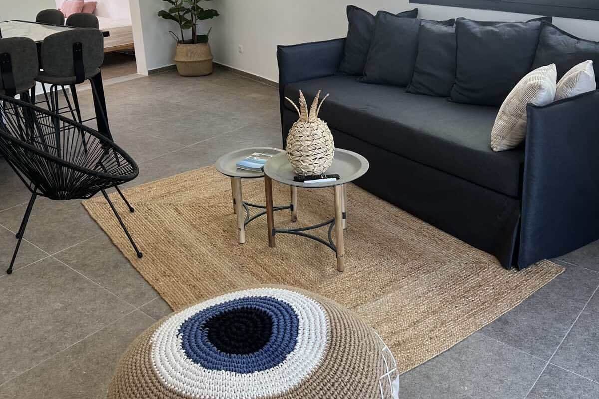 Un salon moderne avec un canapé bleu foncé, un pouf rond en fibres tressées, une petite table basse et une plante en pot.