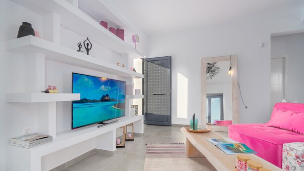 Un soggiorno moderno con una TV a schermo piatto, scaffali bianchi, un divano rosa e un tavolino in legno.