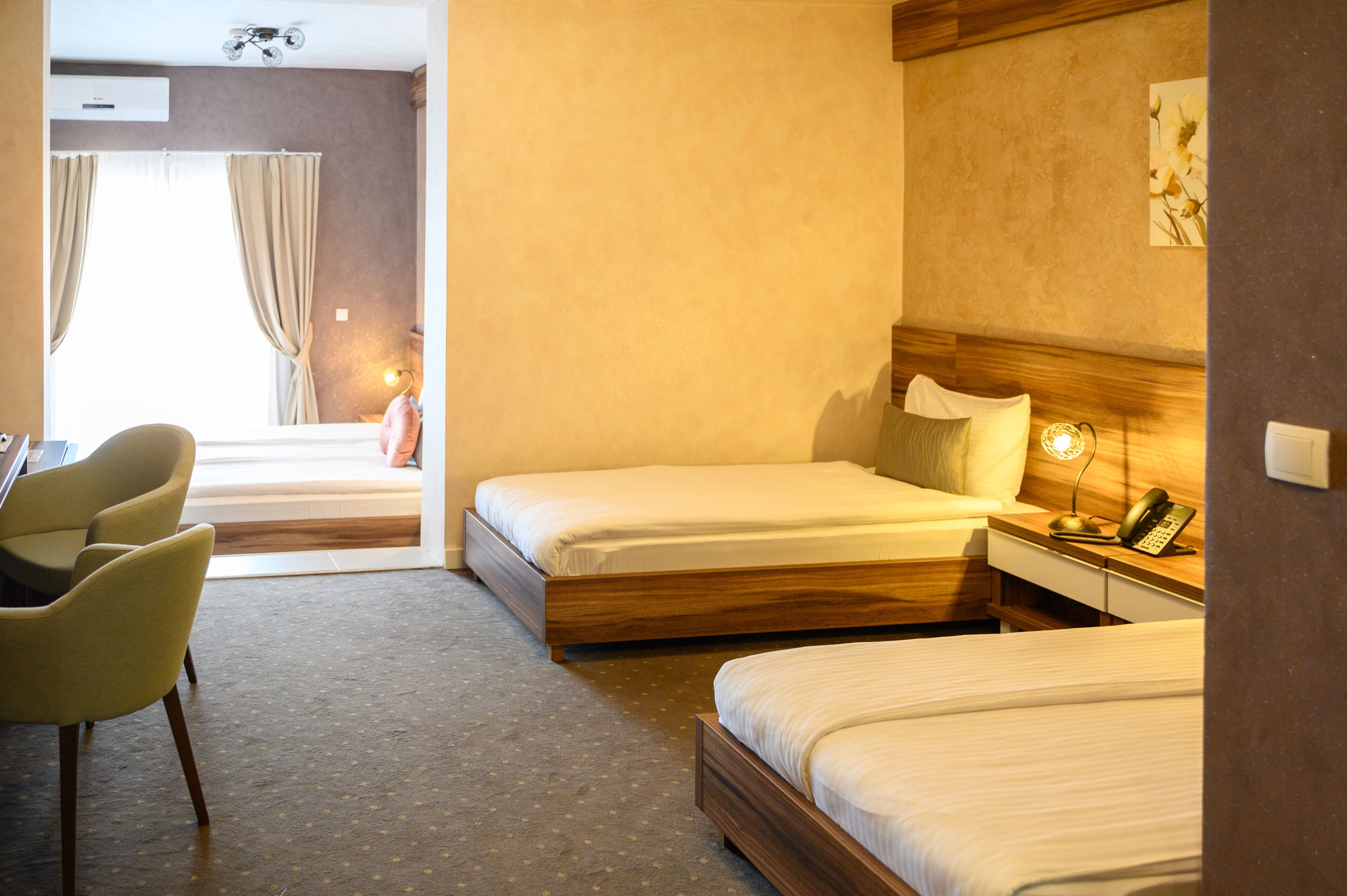 Habitació d'hotel amb dos llits individuals, un escriptori amb cadira, una tauleta de nit amb una làmpada i una finestra amb cortines.