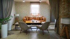 A living room with a leather sofa, two armchairs, a coffee table, and a window with curtains. - Monogram (Inđija)