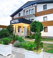 Um hotel com fachada moderna, uma placa indicando ser um hotel Monogram e uma área de jardim bem cuidada na frente.