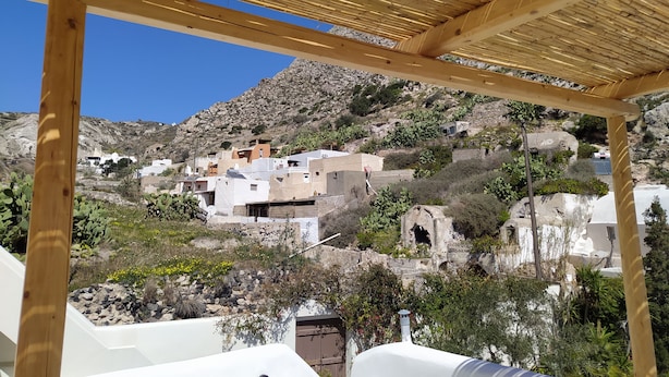 En pergola af træ med udsigt til hvide bygninger på en skråning.
