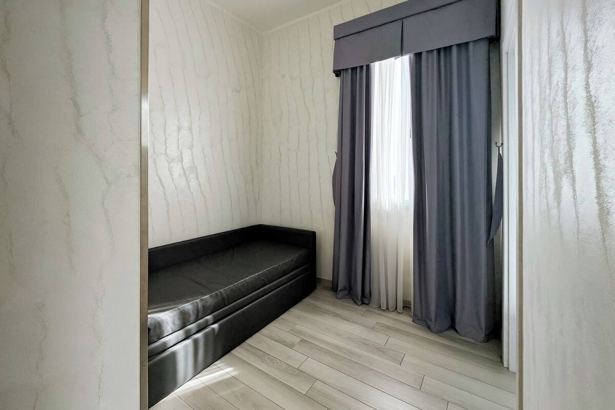 Una habitación pequeña con un banco incorporado, una ventana con cortinas grises y suelo de madera clara.