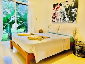 A bedroom with a bed, a window, a painting, and a plant.