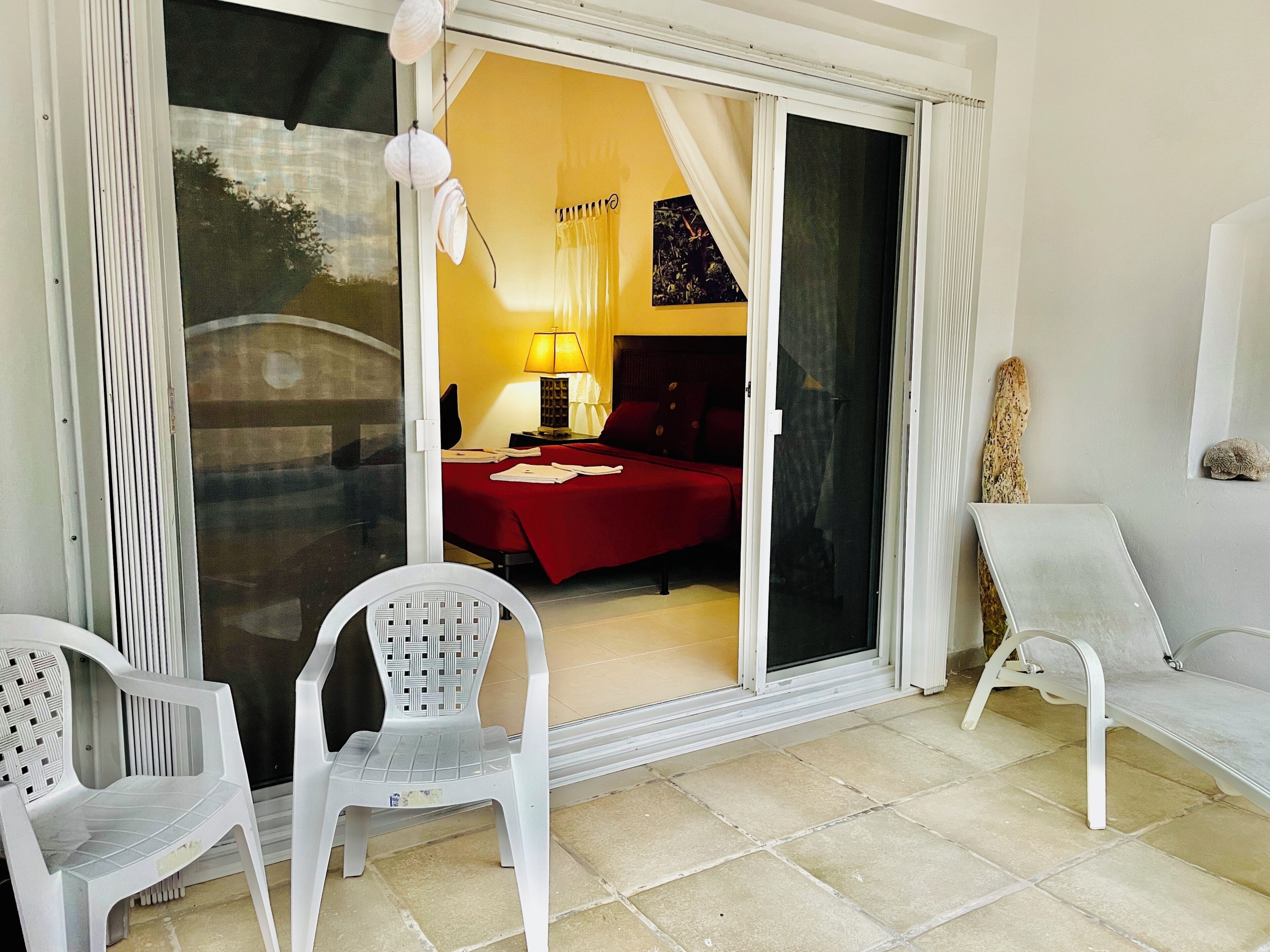 A room with a bed, a chair, a table, and a sliding glass door leading to a balcony.
