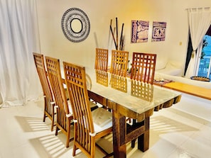 A dining area with a wooden table and chairs, a decorative wall piece, and a view through a window.