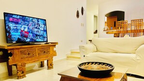 Ein Wohnzimmer mit Fernseher auf einer Holzkommode, einem weißen Sofa und einer dekorativen Schale auf einem Glastisch.