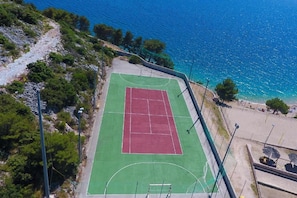 Ein Tennisplatz im Freien neben einem Strand mit freiem Blick auf das Meer.