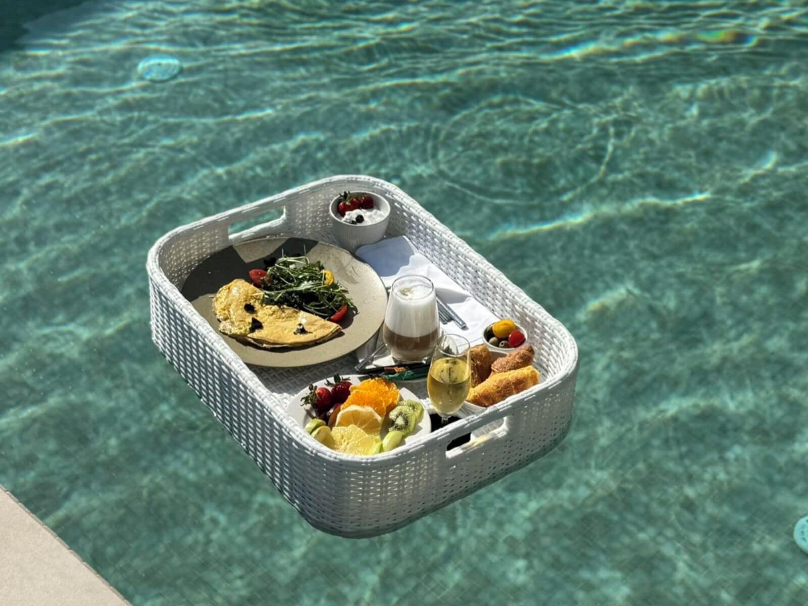A floating dining tray with food and drinks over a pool.