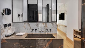 A modern bathroom with a large sink, a mirror, and a TV mounted on the wall.