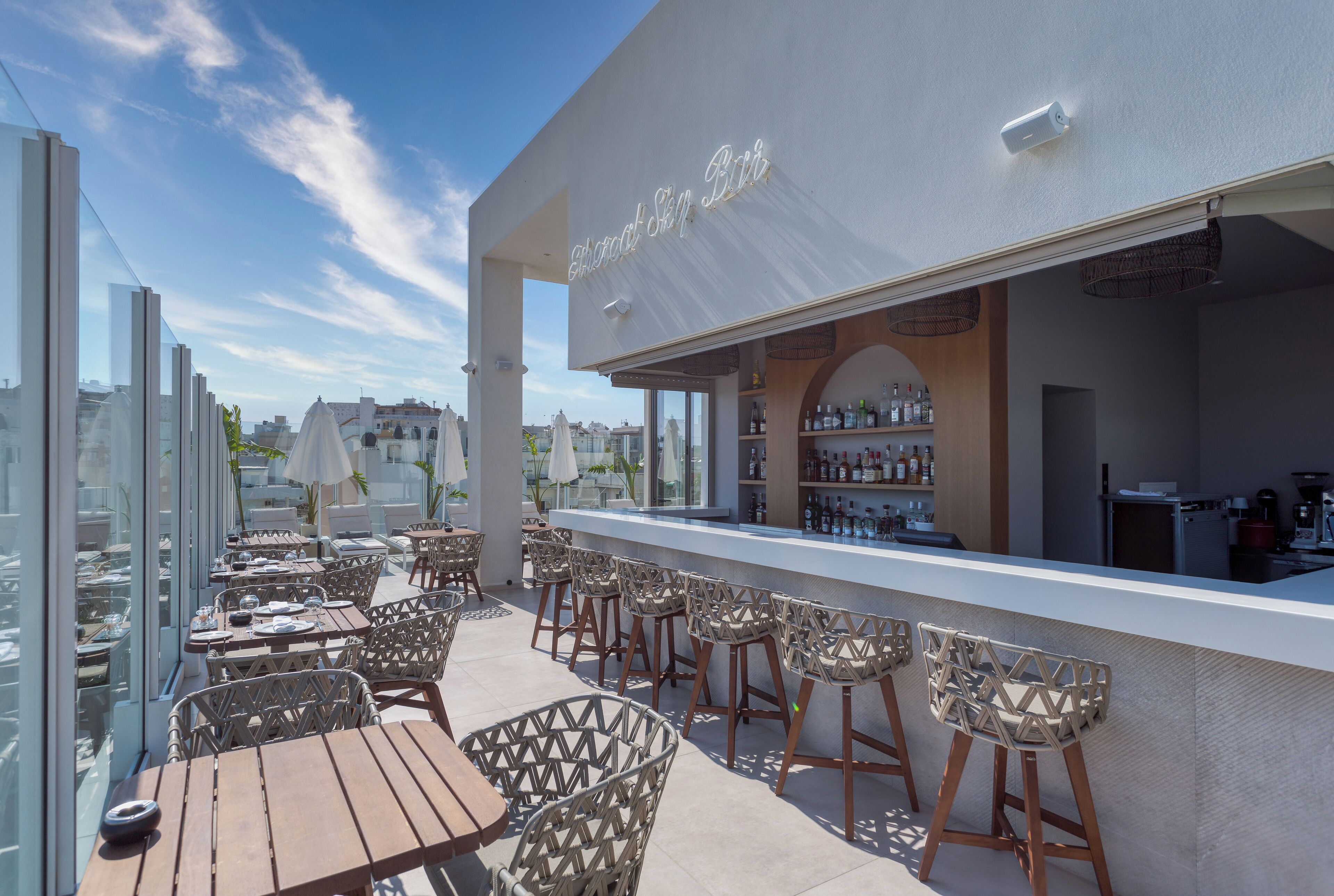 Un bar en la azotea con mesas y sillas altas, una barra y vistas de la ciudad.