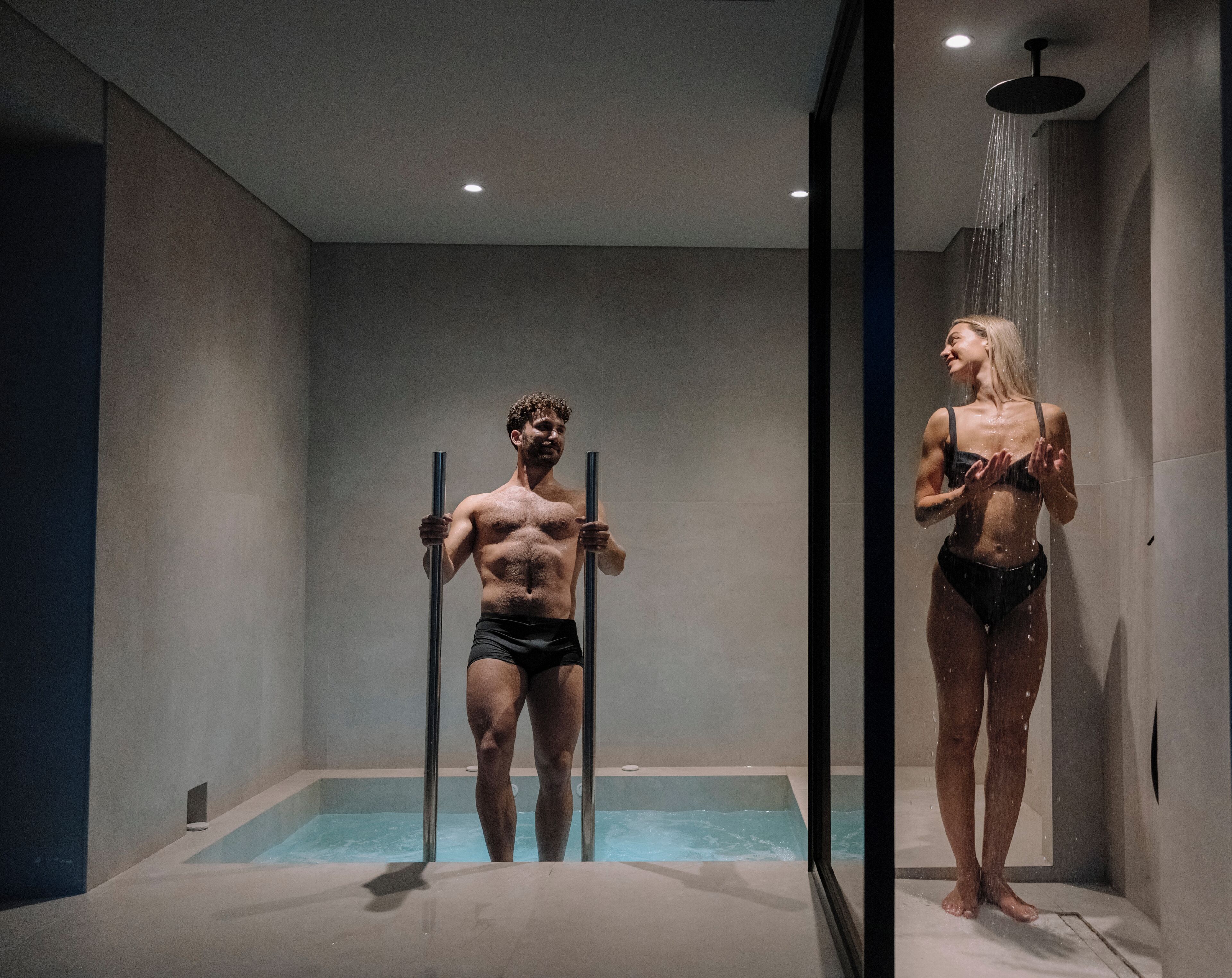 Een moderne badkamer met een glazen jacuzzi, een douchekop en een grote spiegel.