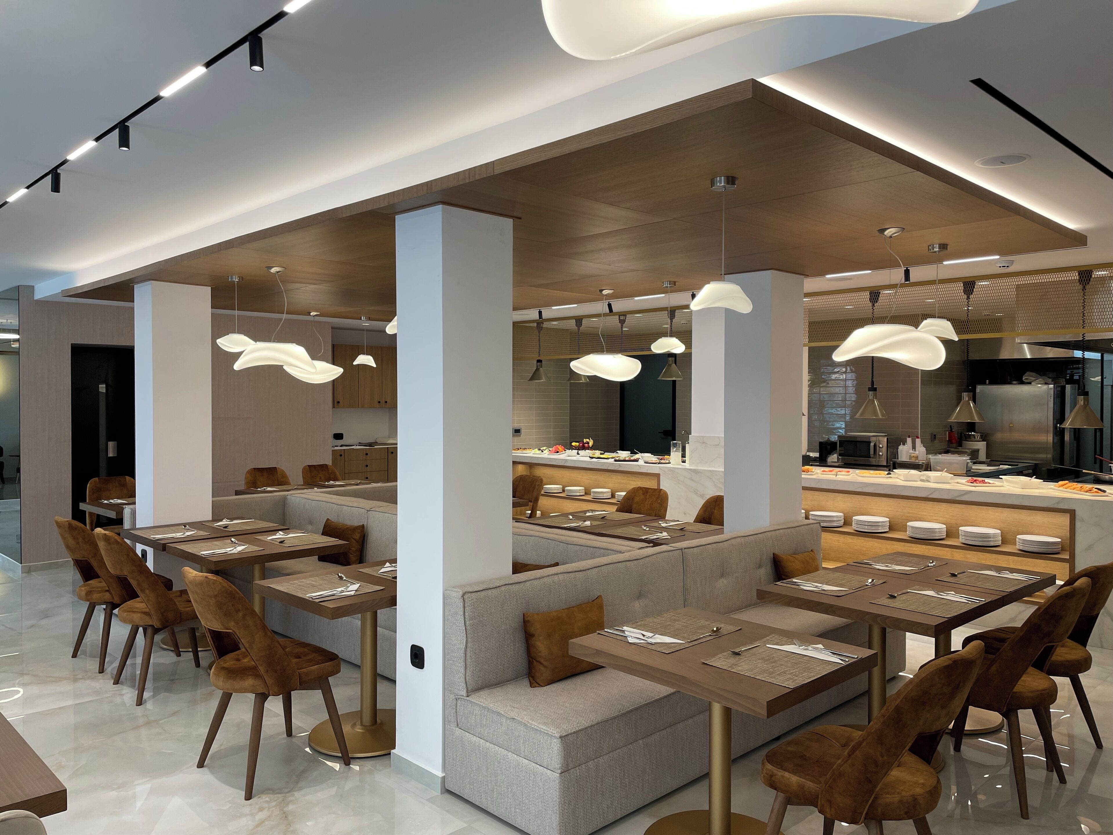 Un restaurant moderne avec des tables hautes et des banquettes, des luminaires suspendus et une cuisine ouverte.