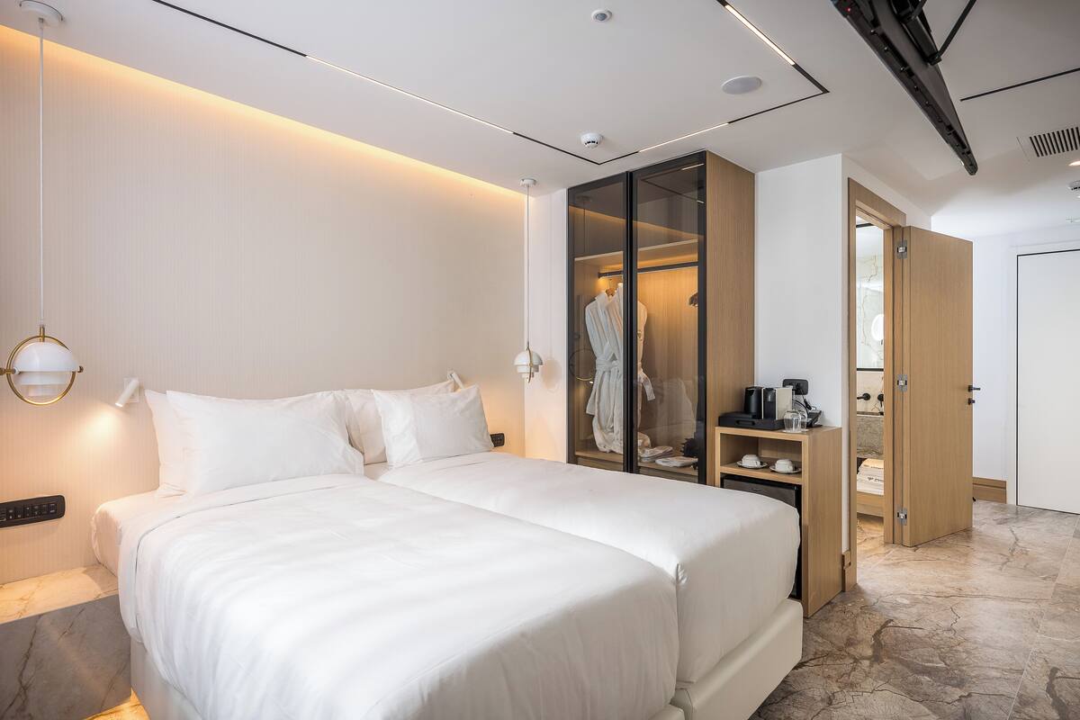 Une chambre d’hôtel moderne avec un grand lit, une armoire avec un miroir et une table de chevet avec une lampe.