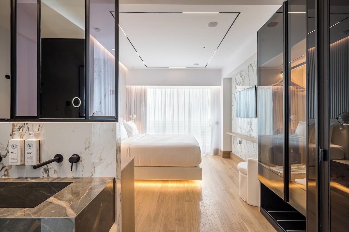 Une chambre d’hôtel moderne dotée d’un grand lit, d’une salle de bain en marbre et d’une douche à parois de verre.