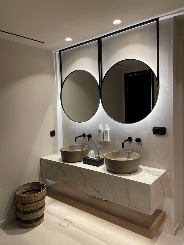 A modern bathroom with two round mirrors, a marble vanity, and a small wicker basket.