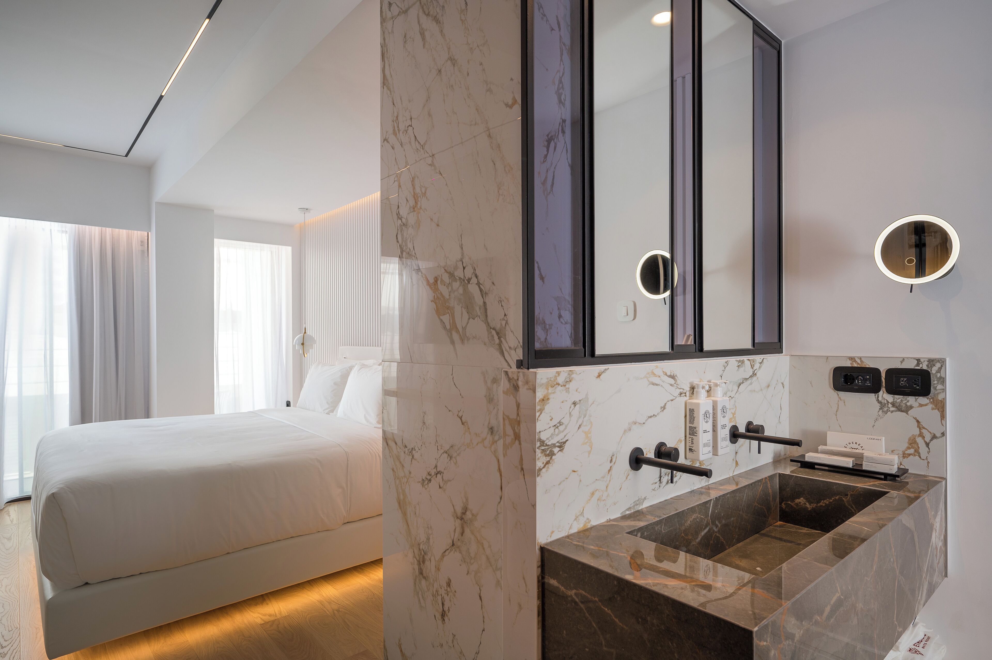 A modern hotel room with a large bed, a marble bathroom vanity, and a large mirror.