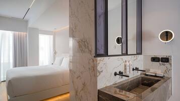A modern hotel room with a large bed, a marble bathroom vanity, and a large mirror.