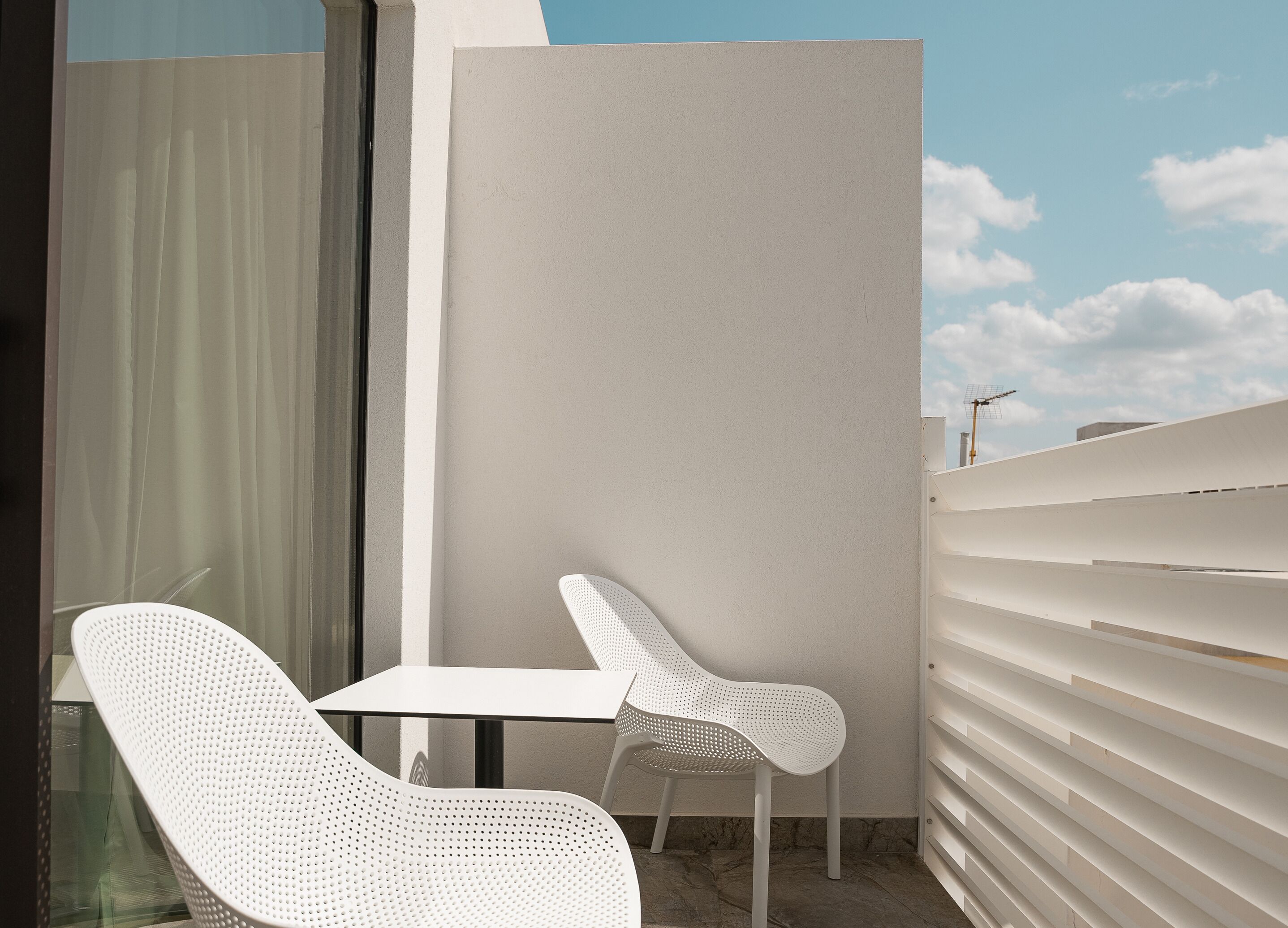 Un área de estar moderna al aire libre con una mesa, dos sillas, un separador de vidrio y una baranda blanca.