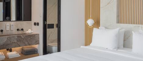 A hotel room with a large bed, a marble bathroom vanity, a mirror, and a wall-mounted light fixture.