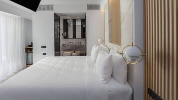 Une chambre d’hôtel moderne dotée d’un grand lit, d’une salle de bain avec un miroir et un lavabo, et d’un téléviseur fixé au plafond.