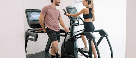 Ein Mann und eine Frau laufen auf Laufbändern in einem Fitnessstudio. Im Hintergrund steht ein weiteres Laufband.