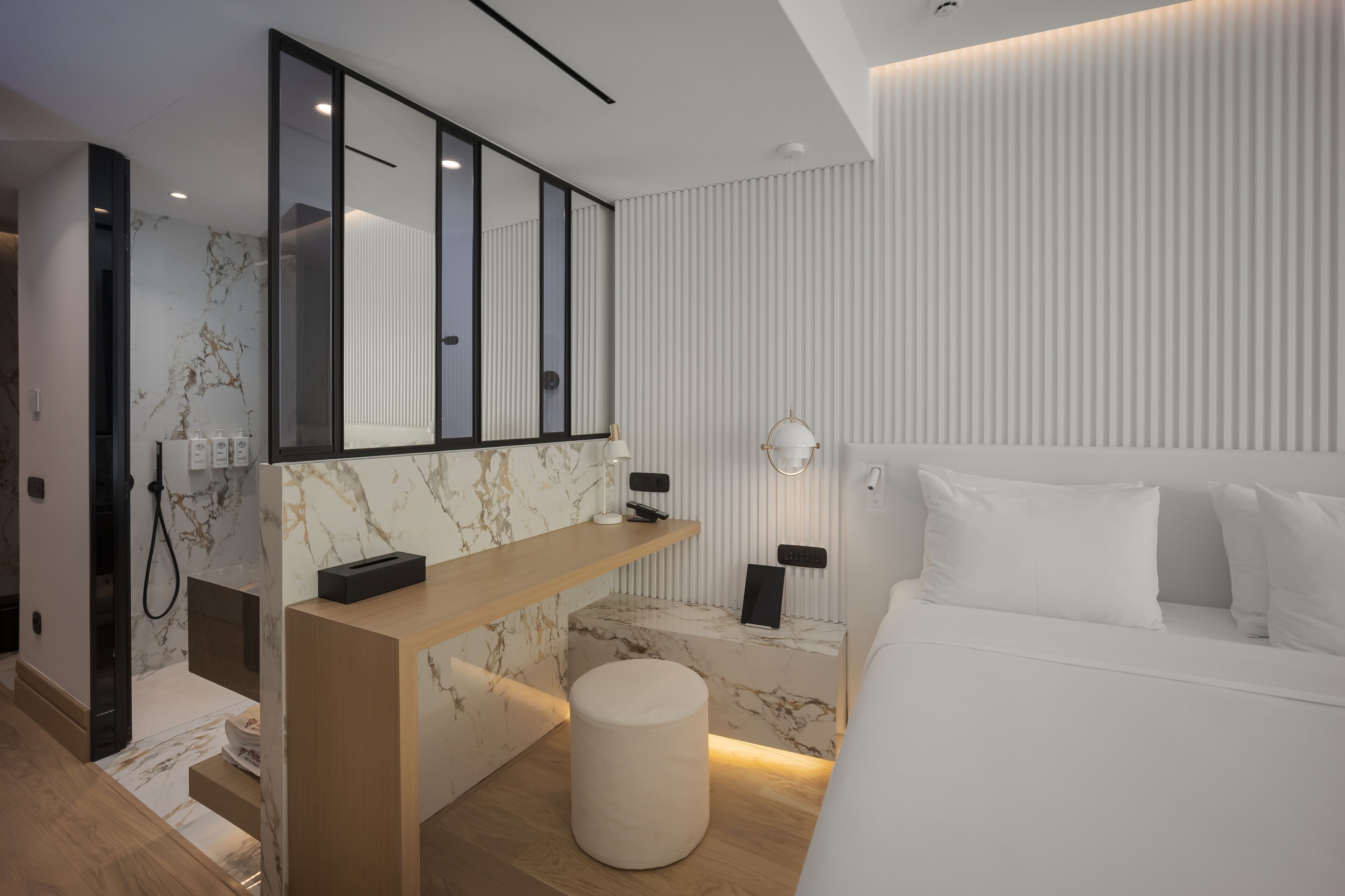 A modern bedroom with a large bed, a marble accent wall, a wooden console table, and a round ottoman.