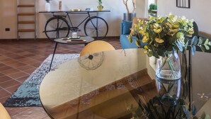 Ein Essbereich mit einem Glastisch, gelben Stühlen, einer Blumenvase, einem Fahrrad und einer an der Wand stehenden Leiter.