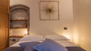 Ein Schlafzimmer mit einem Bett, Kissen, einem an der Wand befestigten Bild, einem Holzschrank und einem Backsteinbogen.
