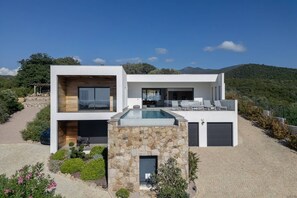 Une maison moderne à deux étages, dotée d’une piscine, d’une façade en pierre et offrant une vue sur les collines environnantes.