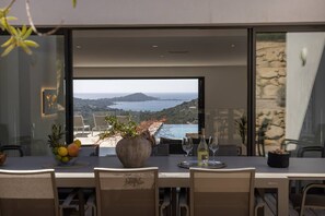 A dining area with a table set for two, a large vase with flowers, and a view of the sea and hills. - VILLA GAIA- 5 bedrooms, swimming pool, sea view (Pietrosella)
