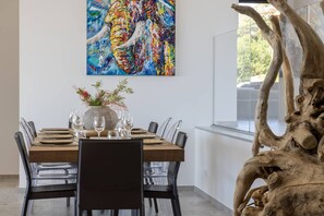 A dining area with a wooden table set for six, surrounded by chairs, a large abstract painting on the wall, and a natural wood sculpture to the right. - VILLA GAIA- 5 bedrooms, swimming pool, sea view (Pietrosella)
