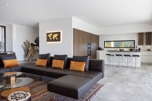 Een moderne woonkamer met een hoekbank, een glazen salontafel en een kamerkleed met dessin.