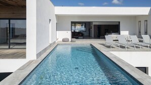 Een modern zwembad met buitengebied, een heldere lucht, een houten terras en ligbedden.