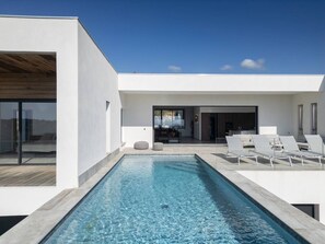 Un espace piscine extérieur moderne, avec un ciel dégagé, une terrasse en bois et des chaises longues.