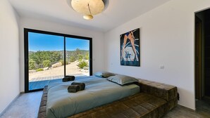 Un dormitorio con un ventanal grande, una cama con almohadas, una obra de arte en la pared y un banco empotrado.