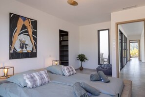 Een moderne slaapkamer met een groot bed, een bijzettafeltje, een vloerlamp, een potplant en een grote spiegel.