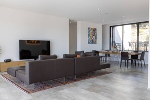 A modern living room with a flat-screen TV, a sofa, and a dining area with a table and chairs.
