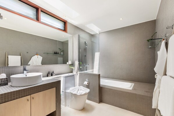 A modern bathroom with a large mirror, a sink, a toilet, and a bathtub.