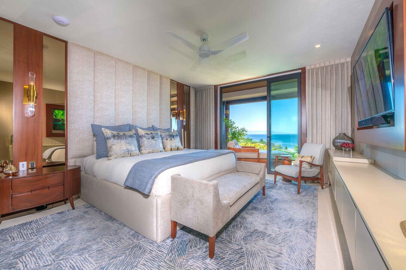 A modern hotel room with a large bed, a seating area, a TV, and a view of the ocean.