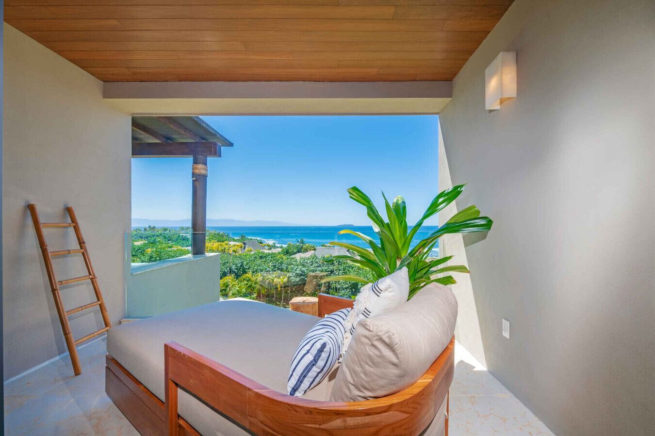 A balcony with a bed, a ladder, and a view of the ocean.