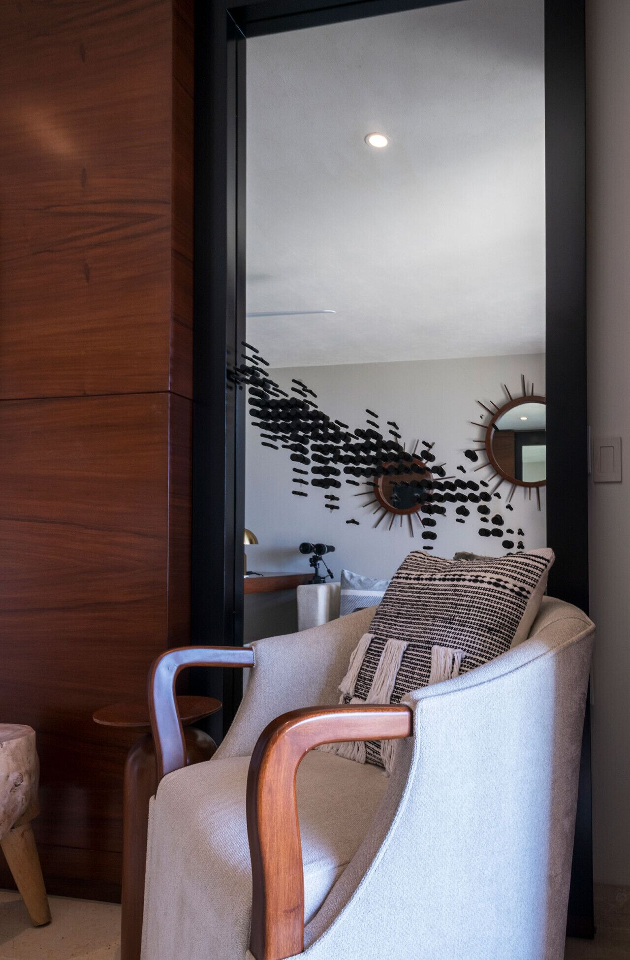 A modern living room with a large mirror, a wooden accent wall, a comfortable armchair, and a unique wall art piece.