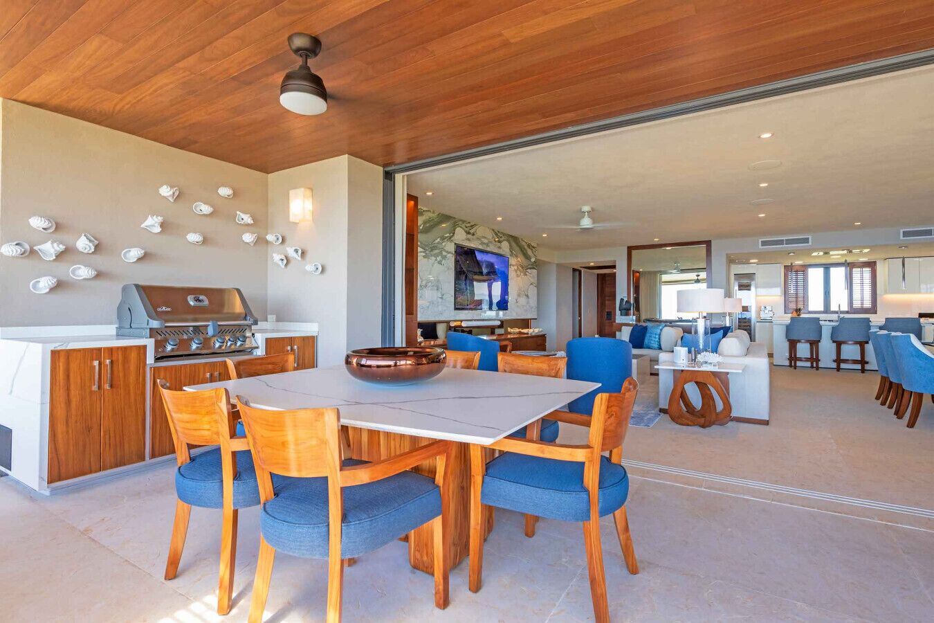 Een ruime woonkamer met een eettafel, blauwe stoelen, een keuken met een grill en een grote televisie.