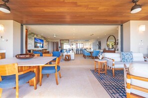 Un vaste espace de vie comprenant une table à manger, des chaises bleues, un canapé blanc et une cuisine en arrière-plan.