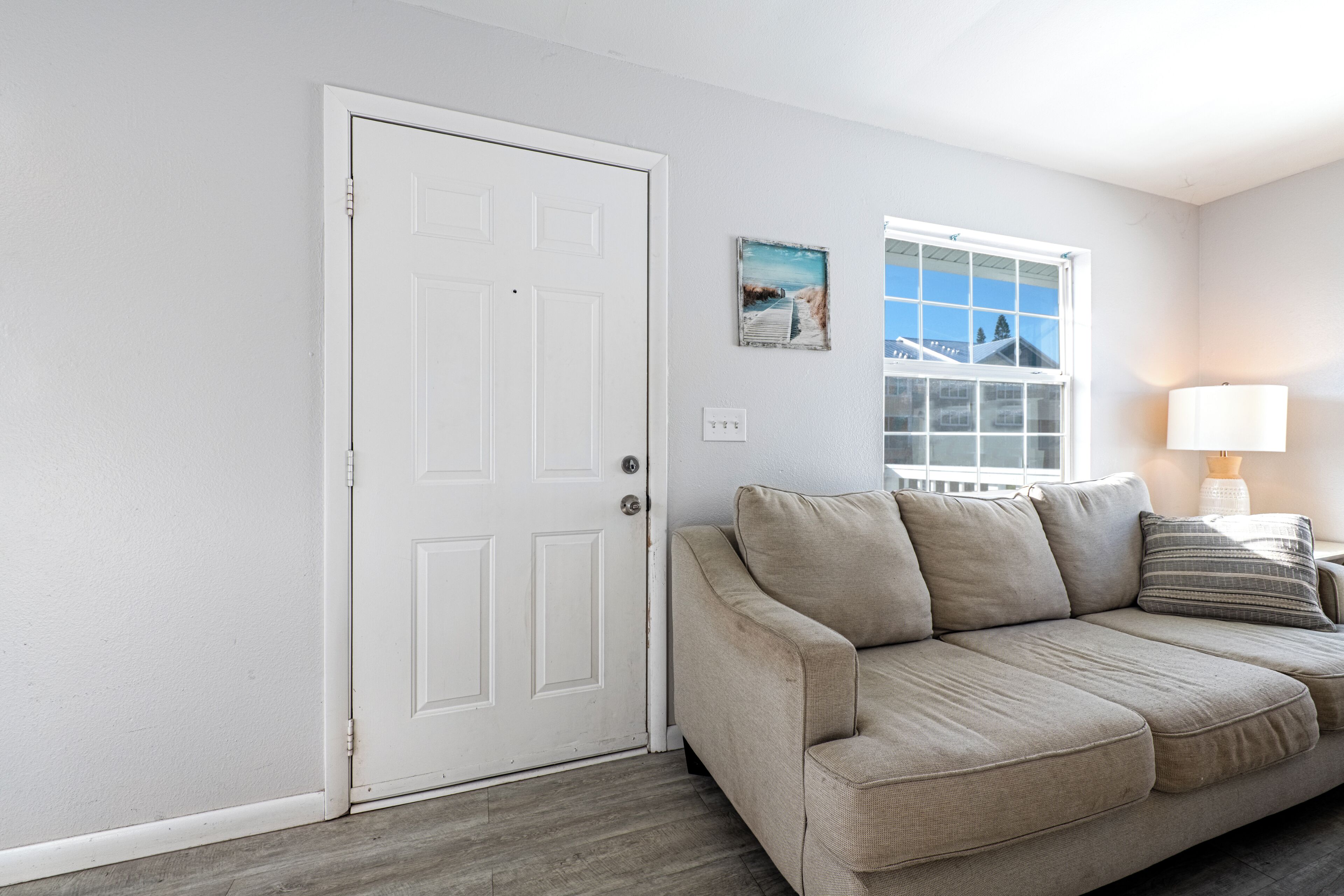 A living room with a beige sofa, a white door, and a window with a view of buildings.