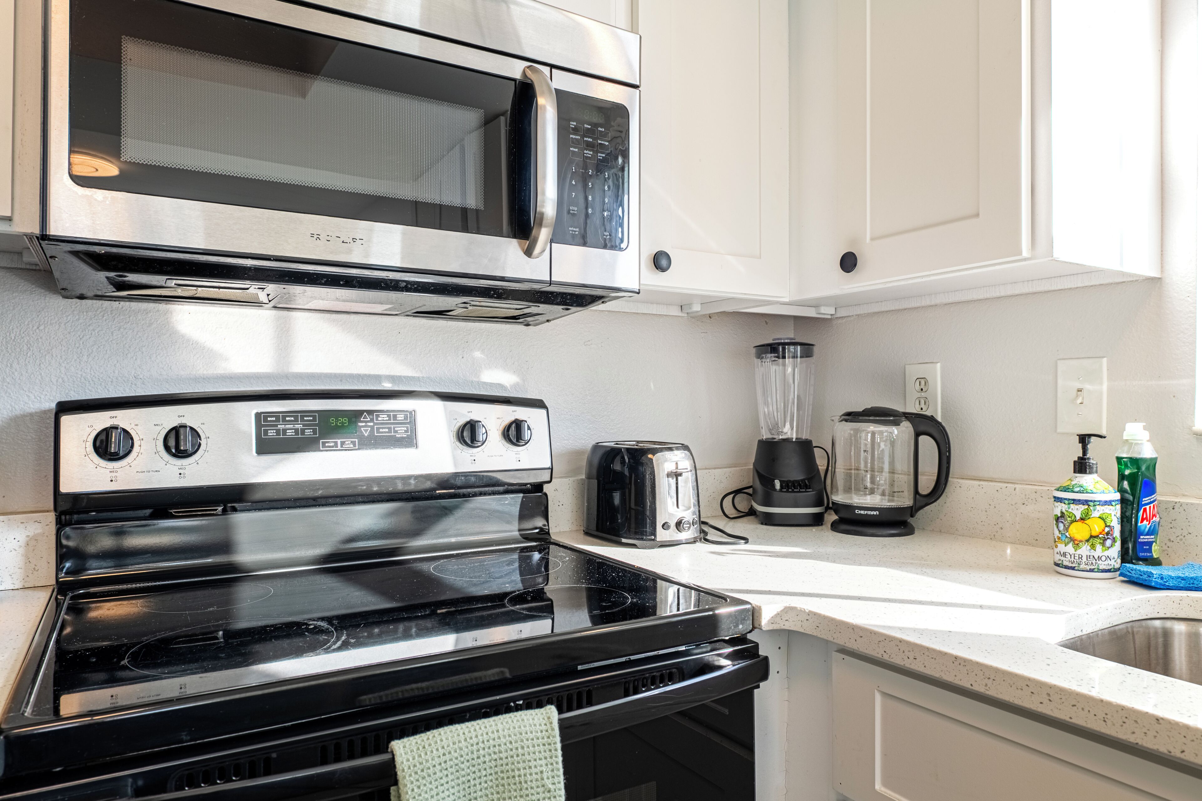 A kitchen with a stainless steel microwave, a stove, a toaster, a blender, and a coffee maker.