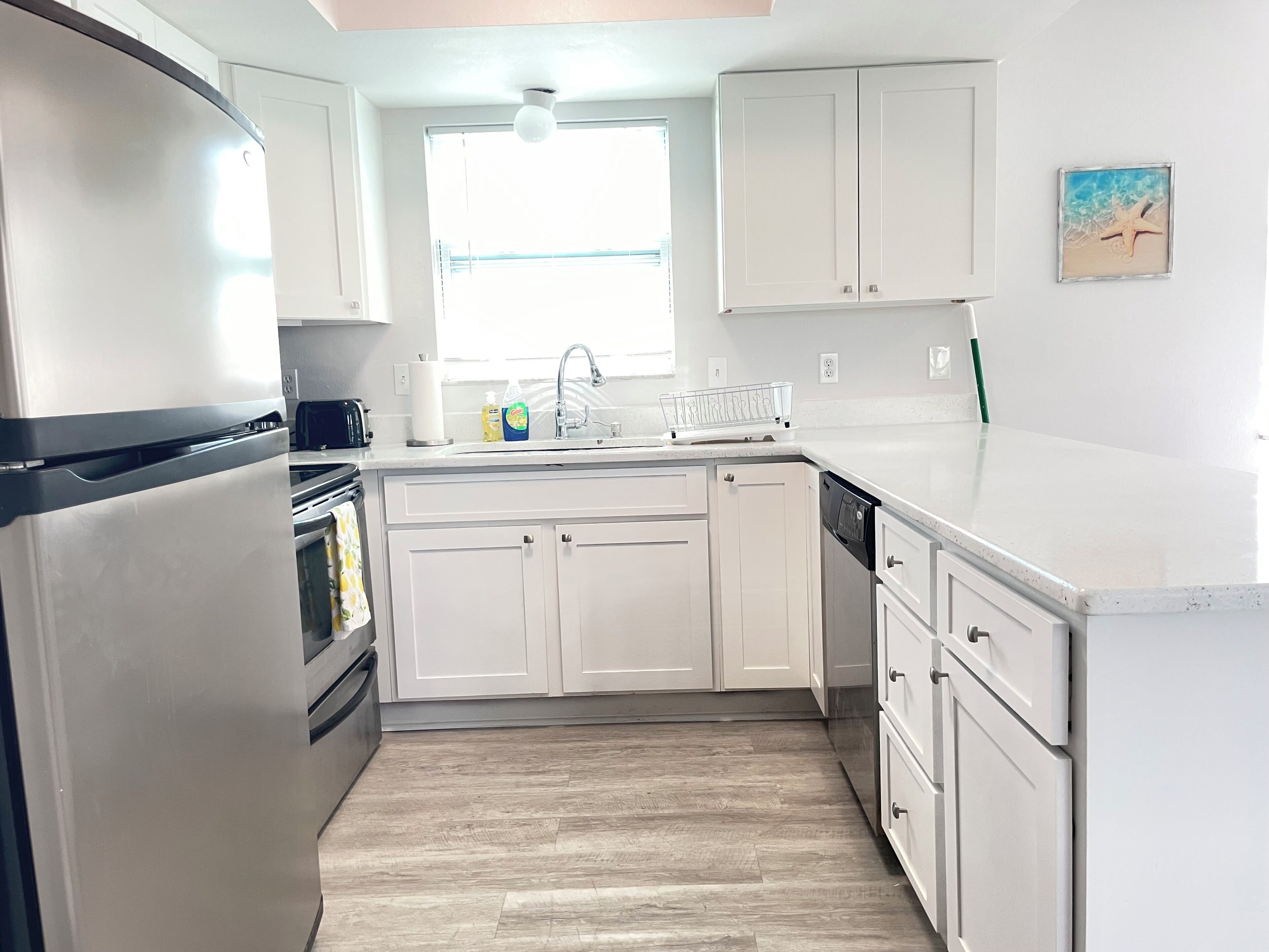 Una cocina moderna con armarios blancos, un refrigerador de acero inoxidable, un lavavajillas y un ventanal que ofrece luz natural.