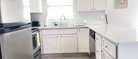 Una cocina moderna con armarios blancos, un refrigerador de acero inoxidable, un lavavajillas y un ventanal que ofrece luz natural.