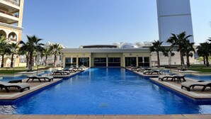 A swimming pool with lounge chairs, a building with balconies, and a tall skyscraper in the background. - Marina Residence 1004 (Dubai)