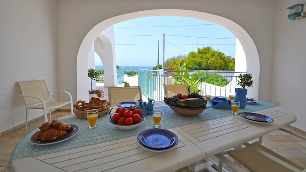 A dining table with breakfast items, a view of the sea, and a balcony with a railing and plants. - 3241 Villa Esador by Barbarhouse (Racale)